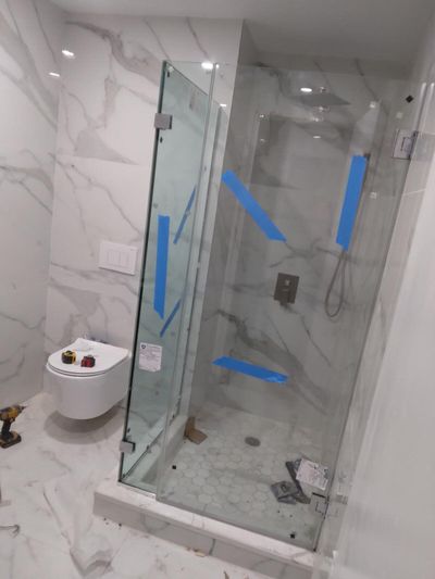 Corner glass shower enclosure, marble-look wall tile, and wall-mounted toilet