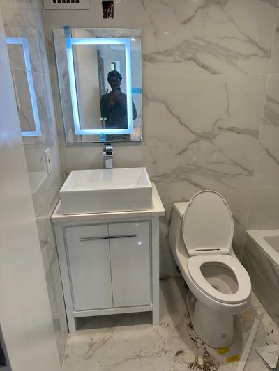 White vanity, vessel sink, illuminated mirror, and marble-look wall tile