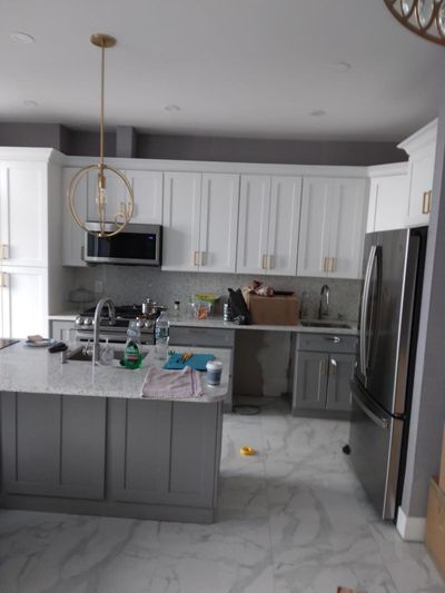Kitchen with white upper cabinets, gray island, and stainless steel refrigerator
