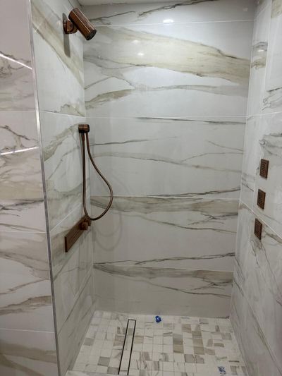 Walk-in shower with marble-look wall tile, mosaic floor, and bronze fixtures