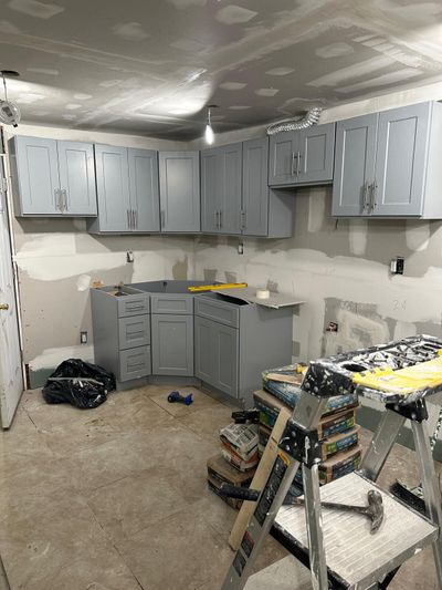 Gray wall cabinets, unfinished drywall, and stepladder during kitchen work